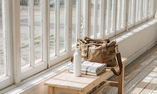 A canvas gym bag, a water bottle and a folded towel resting on a wooden bench in late golden hour light.