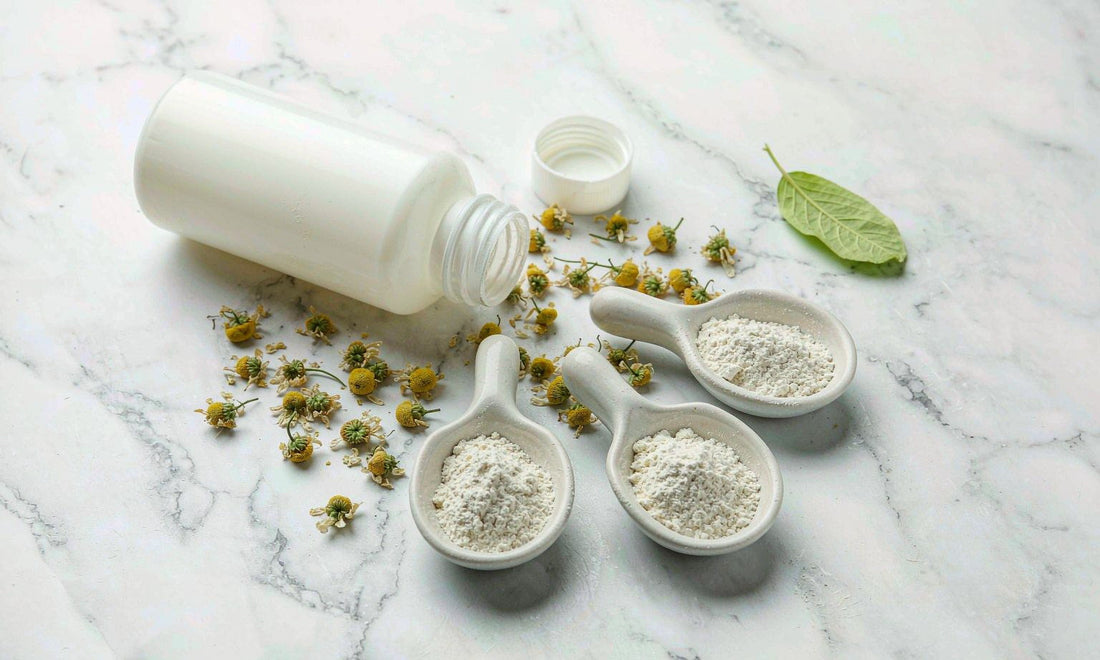 Overhead flat lay of a blank supplement bottle, chamomile flowers and powder bowls on marble
