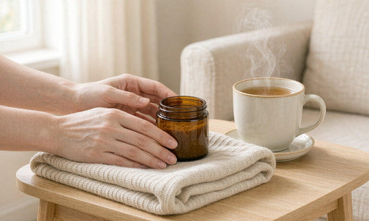 Fair-skinned hands holding a small amber jar beside a steaming cup of herbal tea in daylight