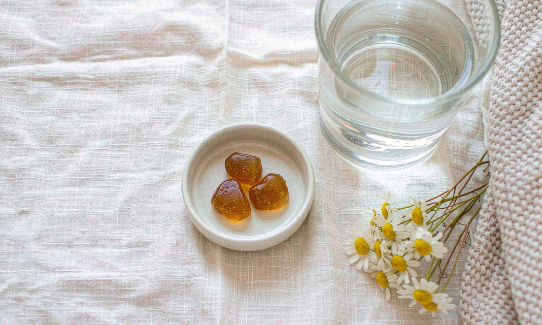 Amber magnesium gummies in a ceramic dish with dried chamomile and water on cream linen.