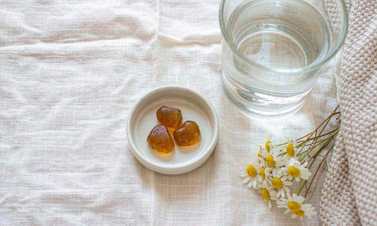 Amber magnesium gummies in a ceramic dish with dried chamomile and water on cream linen.