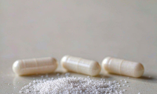 Extreme macro of white crystalline magnesium powder and three pale capsules on a matte grey surface.