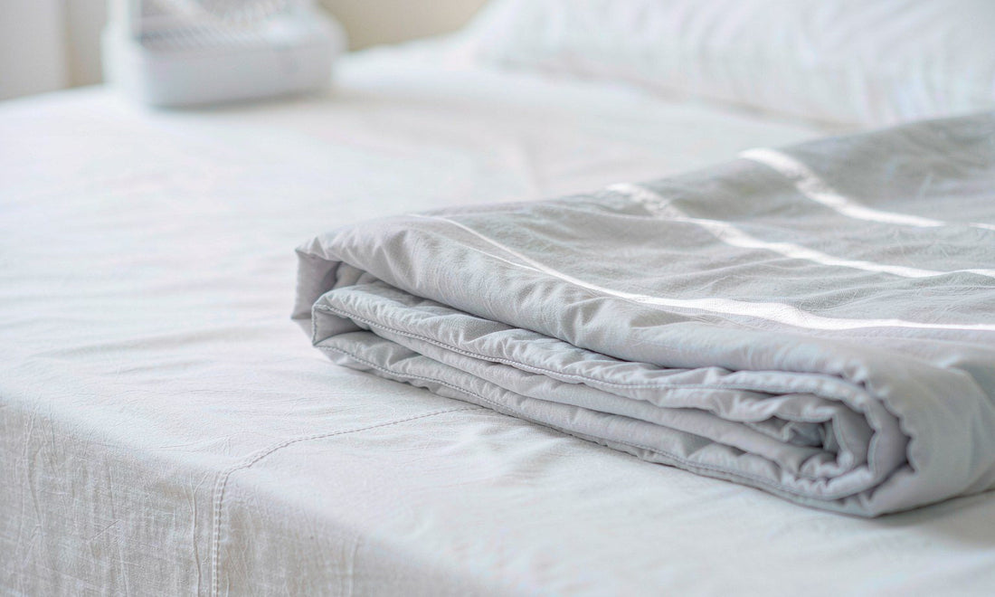 Macro detail of folded pale grey bedding on crisp white sheets in cool soft light