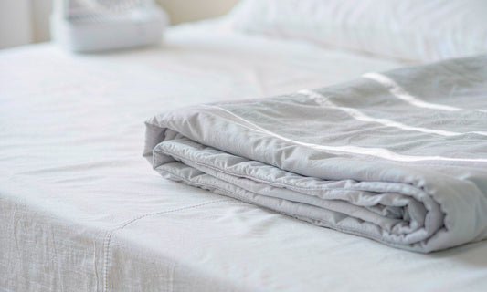 Macro detail of folded pale grey bedding on crisp white sheets in cool soft light
